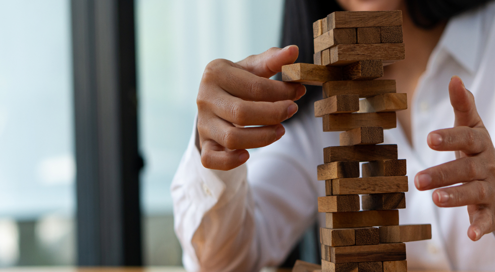 Person in a white shirt carefully removes a wooden block from a tall, unstable stacking tower game.